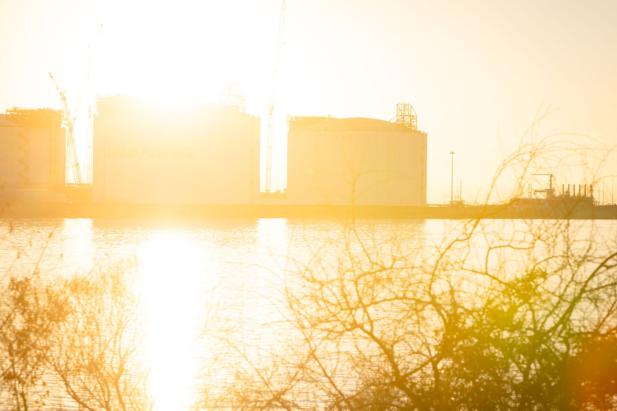 Sunlight streams behind large structures at the Golden Pass LNG Terminal in Port Arthur, TX.