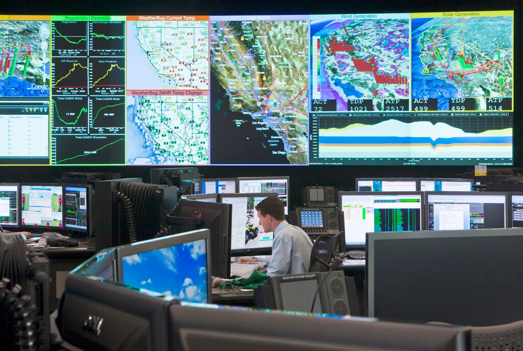 A person in a large room filled with large monitors with maps and data, including some that fill the walls.
