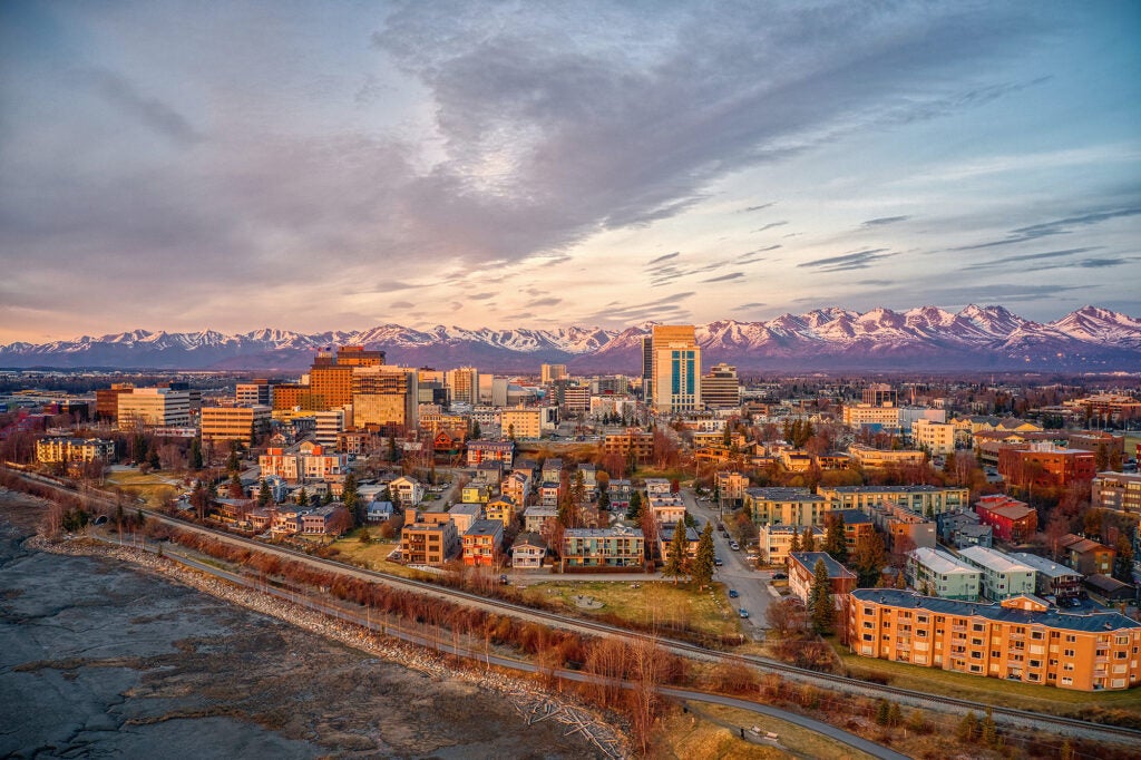 An areal photo of Anchorage, a medium sized city, in the foreground, with snowy mountains in the distance.