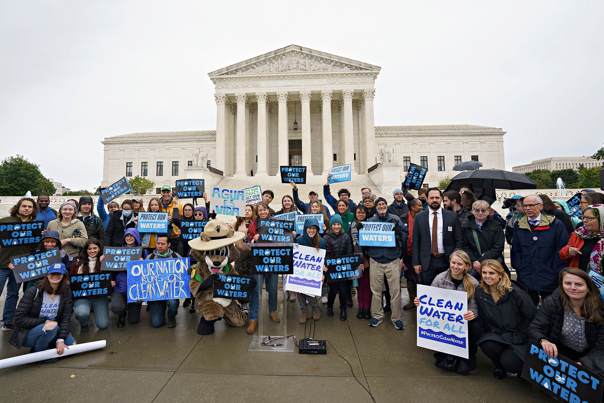 A large group of people hold signs for clean water in front of the Supreme Court Building.