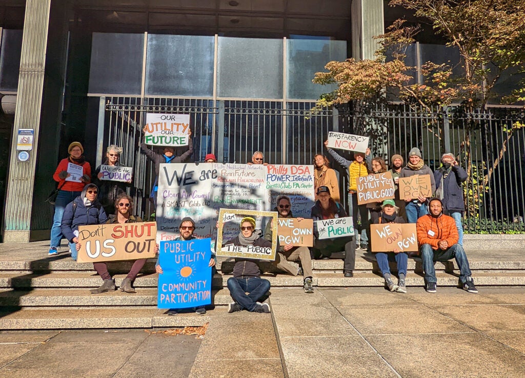 A group of more than a dozen people hold signs advocating for utility reform and climate justice outside of a large office building.