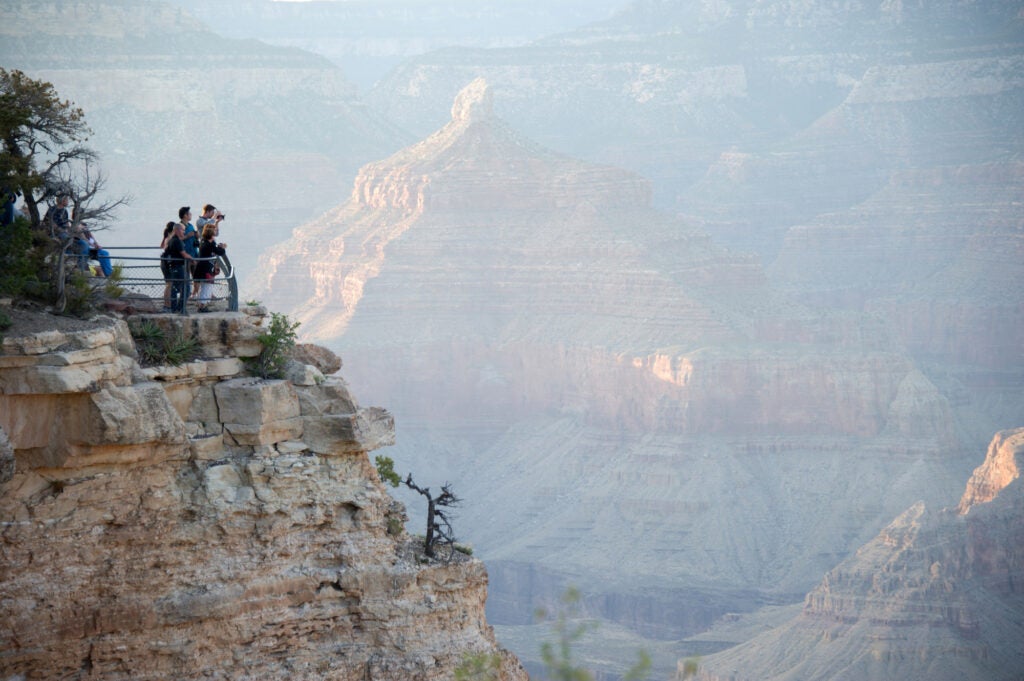 A group of people stand on an observation deck with a hazy and barely visible canyon behind them.