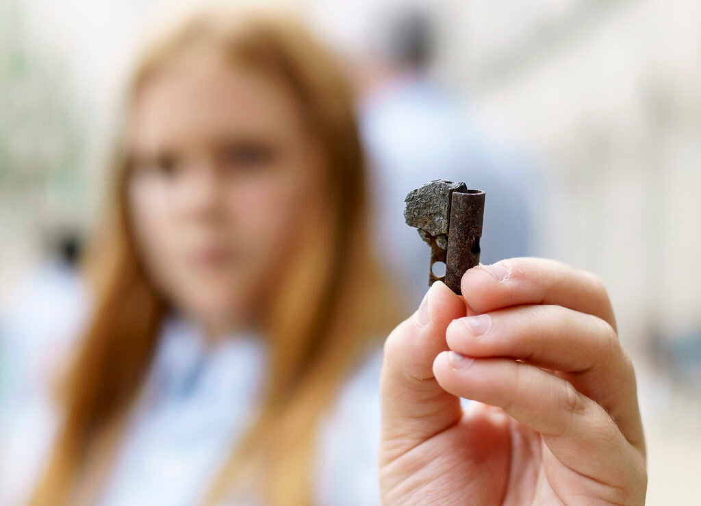 A piece of dark metal in the foreground, being held by a young girl, out of focus in the background.