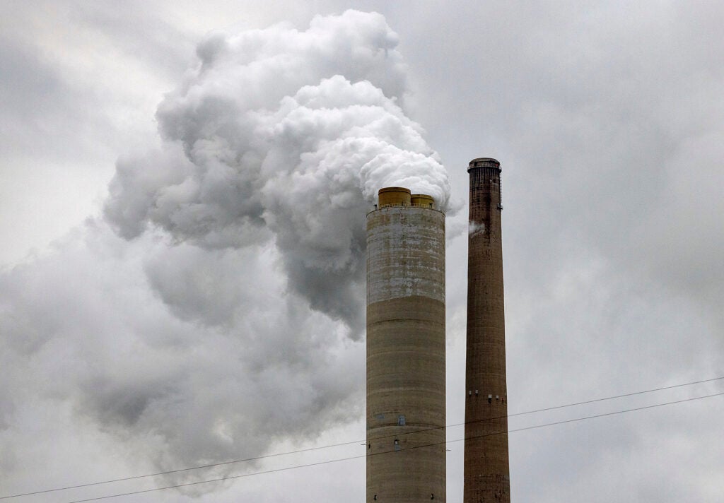 Two smoke stacks against a gray sky. One is releasing a lot of white smoke.