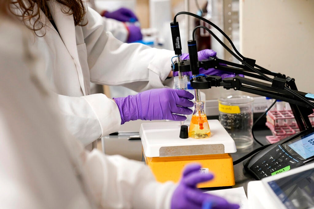 People in lab coats work with scientific equipment with purple gloves on.