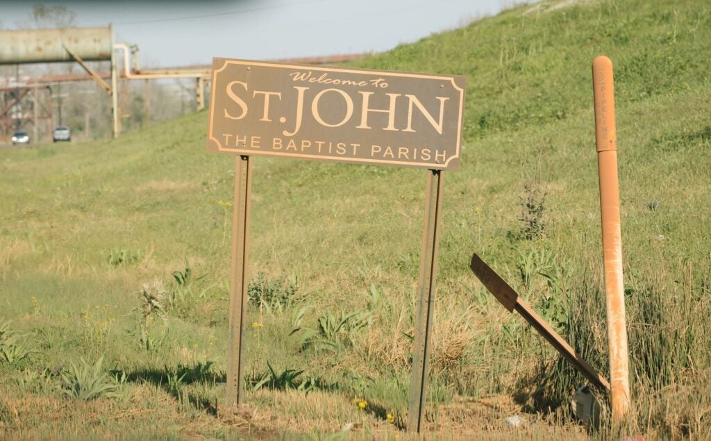 The welcome sign to St. John the Baptist Parish, Louisiana, and a pipeline marker, are covered in red dust from the nearby Atlantic Alumina facility. (Brad Zweerink / Earthjustice)