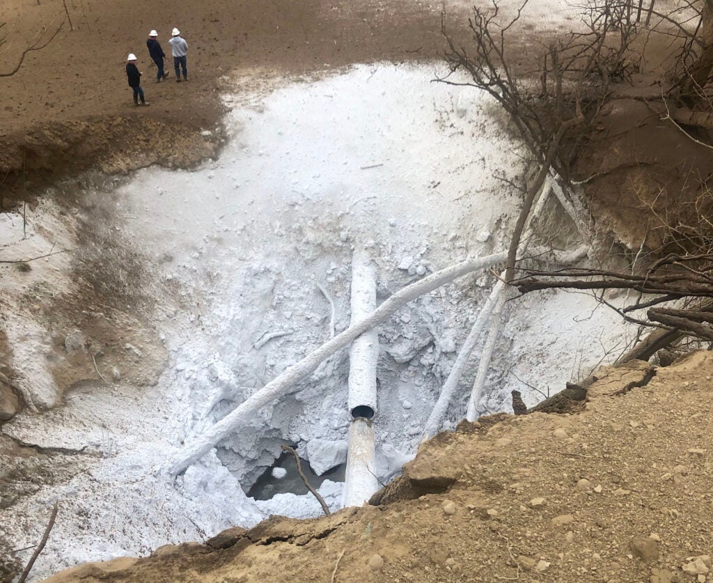 A large hole with a broken pipe in it, covered in a white powder.