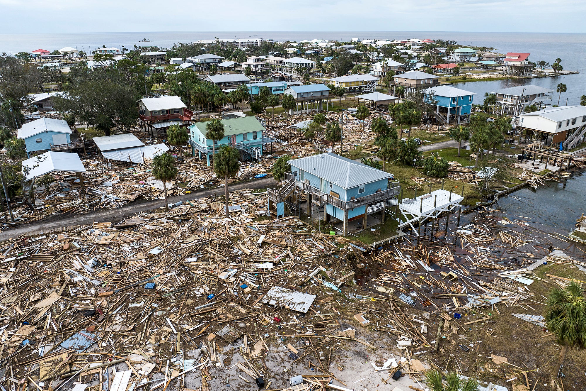 A beachside community with raised up homes, surrounded by debris from other homes that were destroyed by the storm.