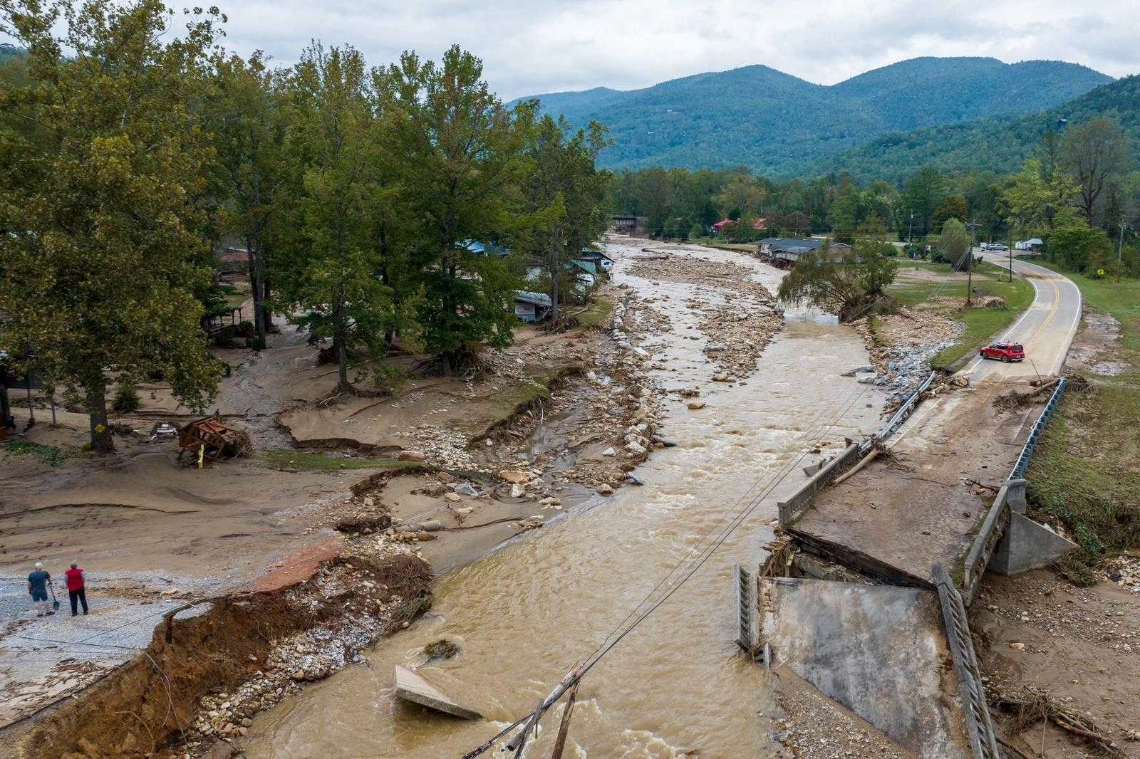 A brown, washed out river with eroded banks with a two-lane bridge in the foreground that has completely collapsed into the water.