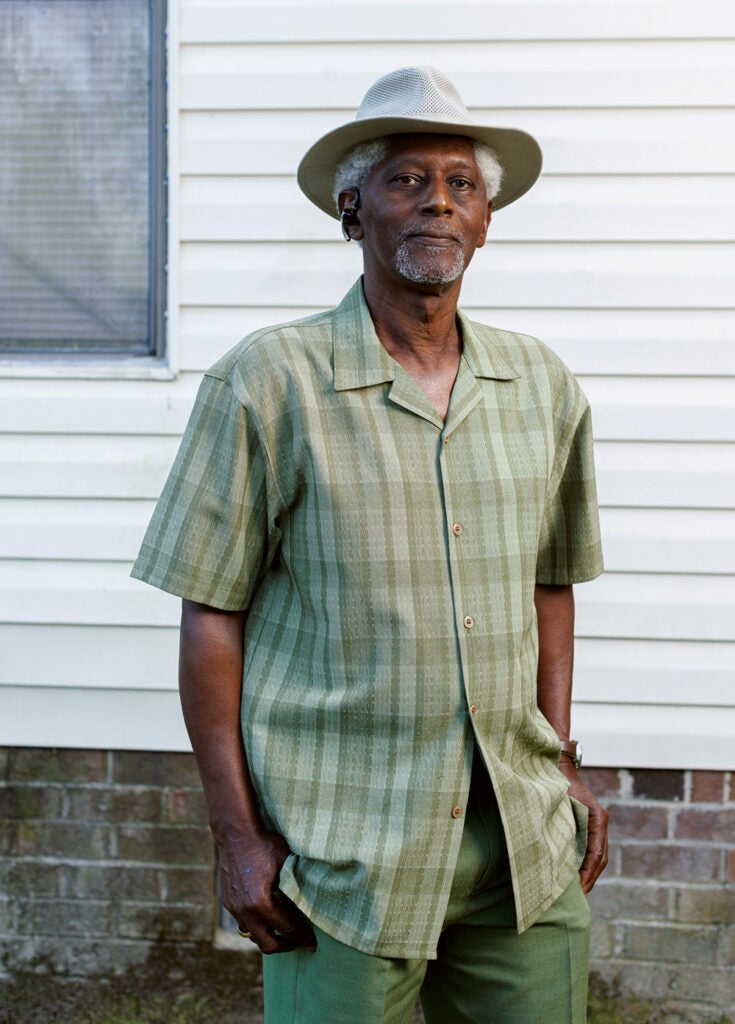 A portrait of a man looking into the camera, wearing a green shirt and hat.