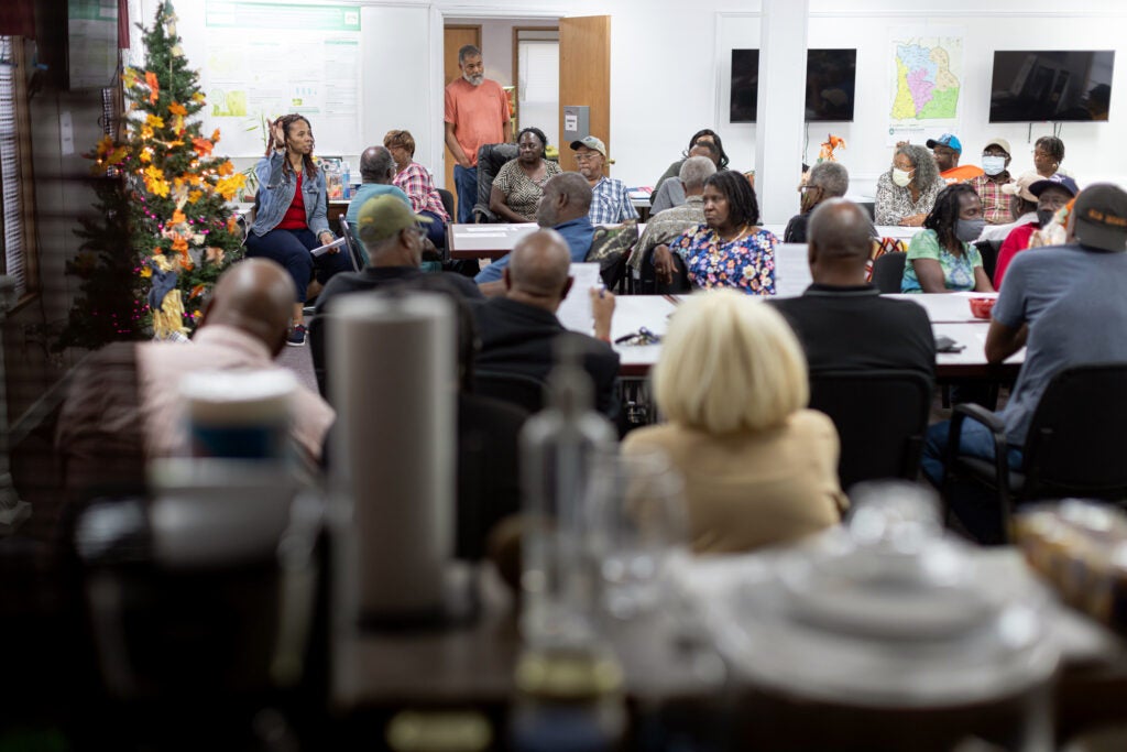 A large meeting room is filled with people listening to a speaker.