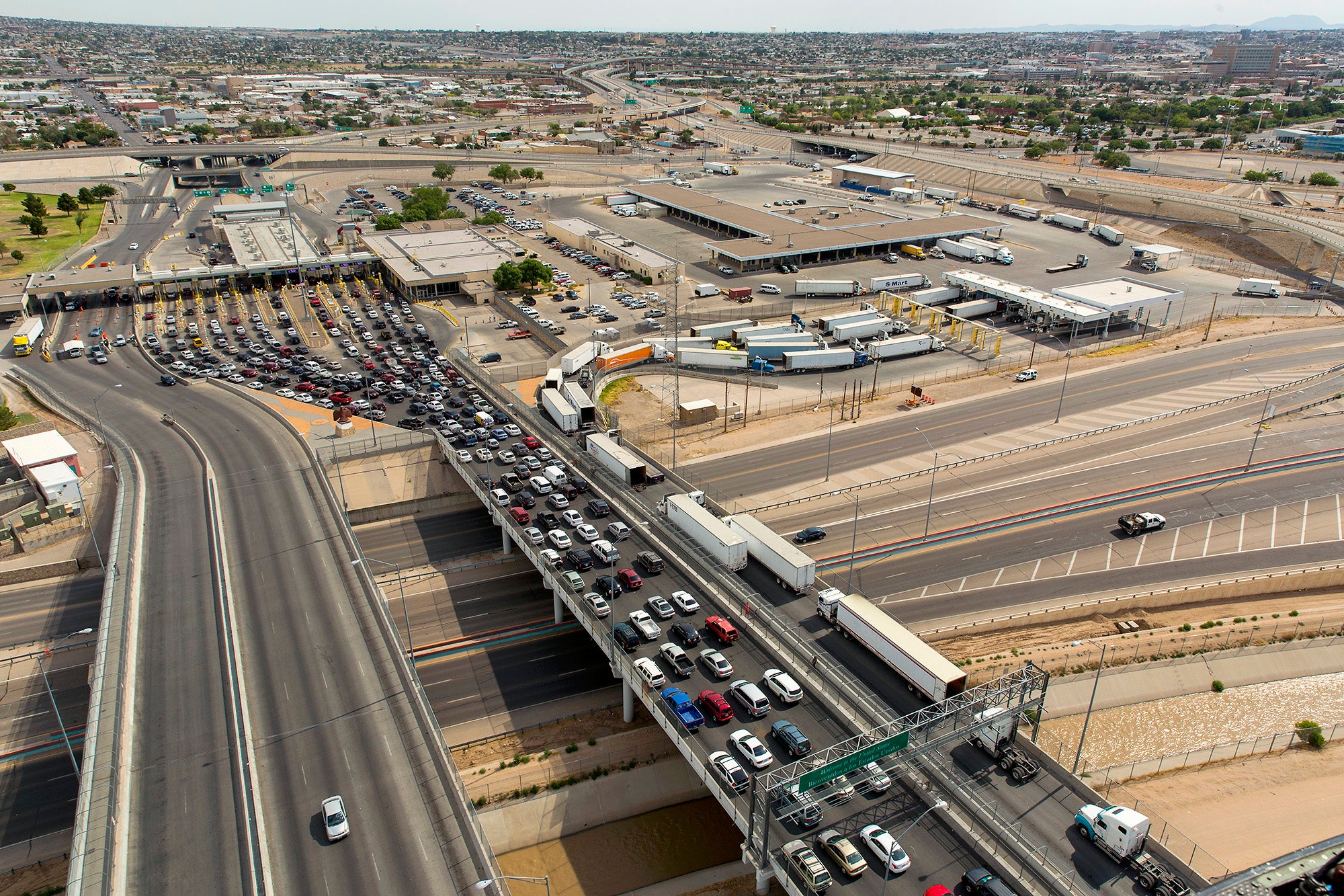 Two bridges over a highway and canal, one filled with cars and trucks, with the city of El Paso in the background.