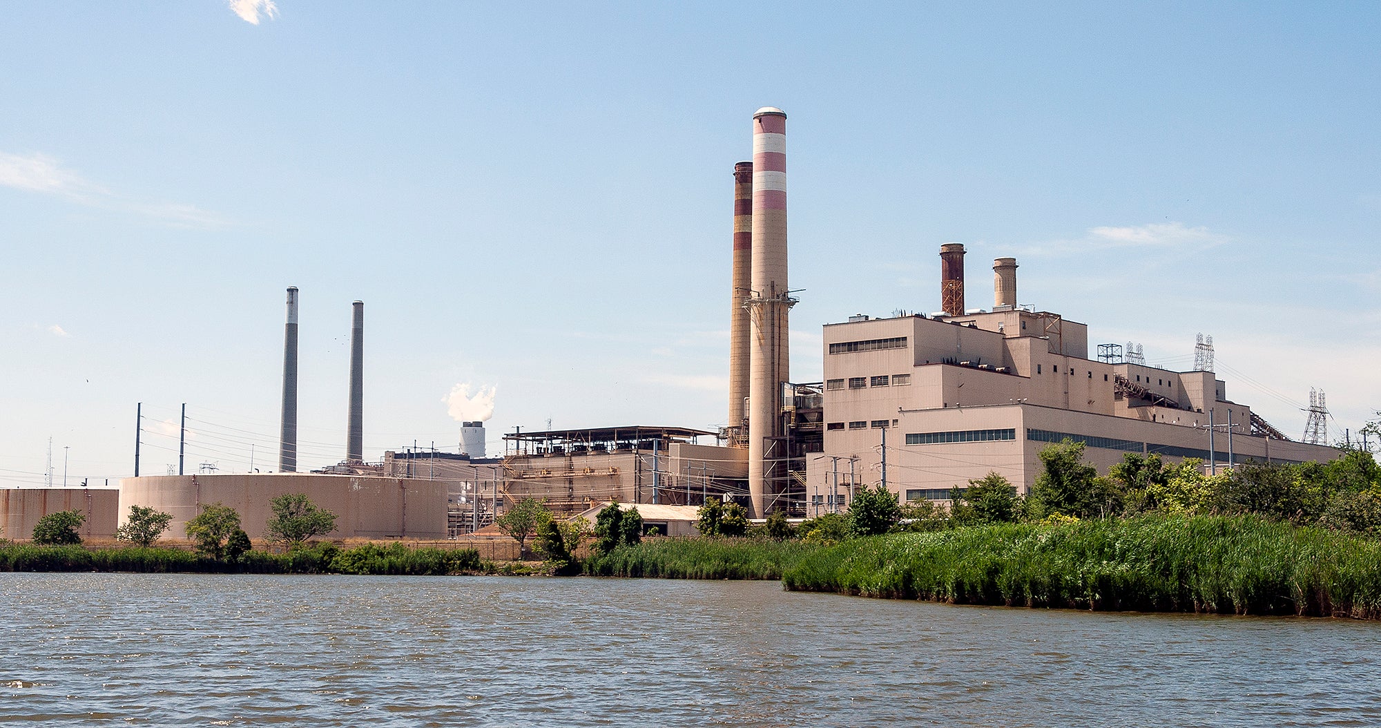 A large, tan power plant with tall smoke stacks next to water.