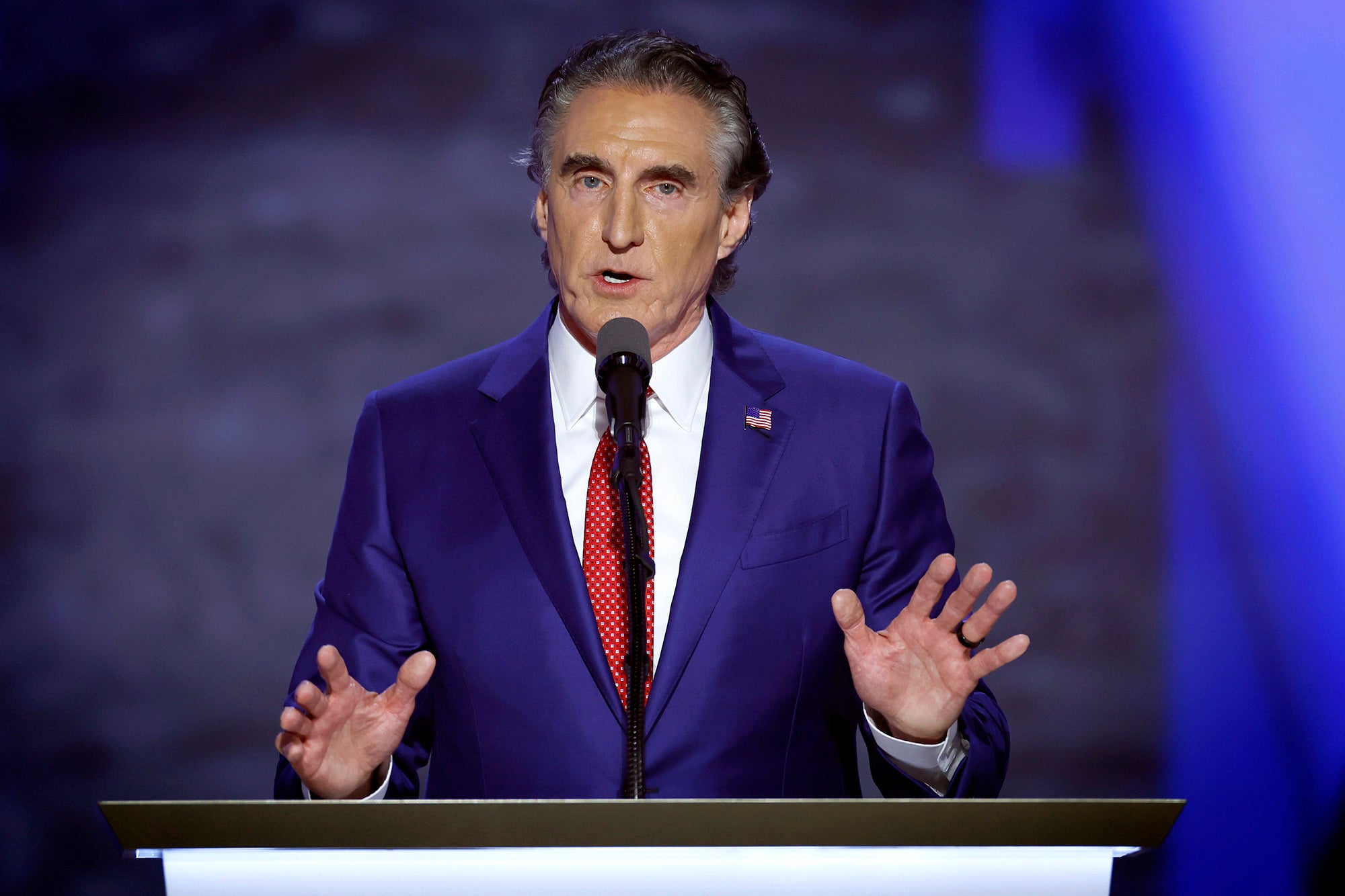 A man in a blue suit speaks at a podium