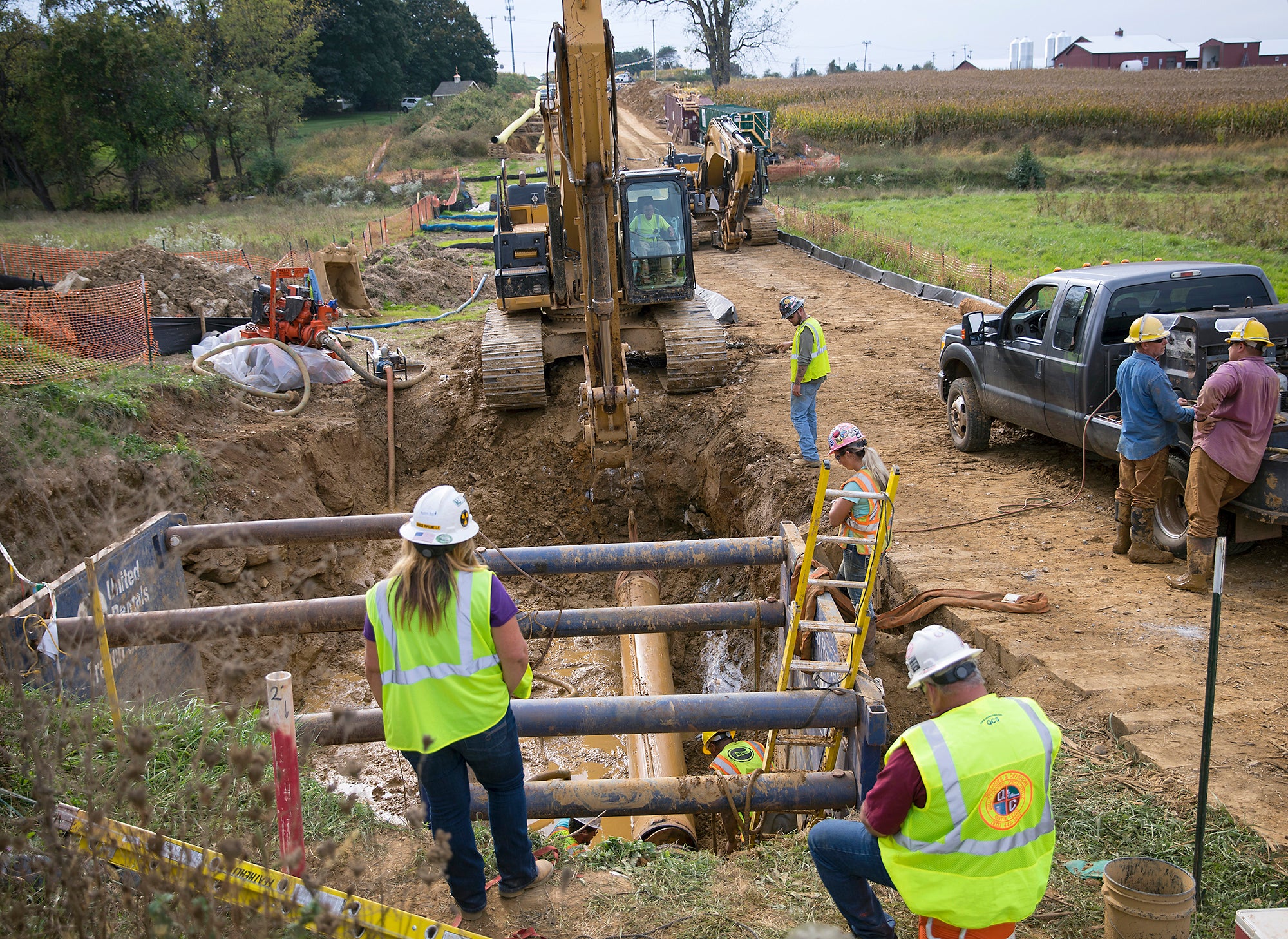 A group of construction workers with heavy equipment work on a pipe in a large hole in the ground.