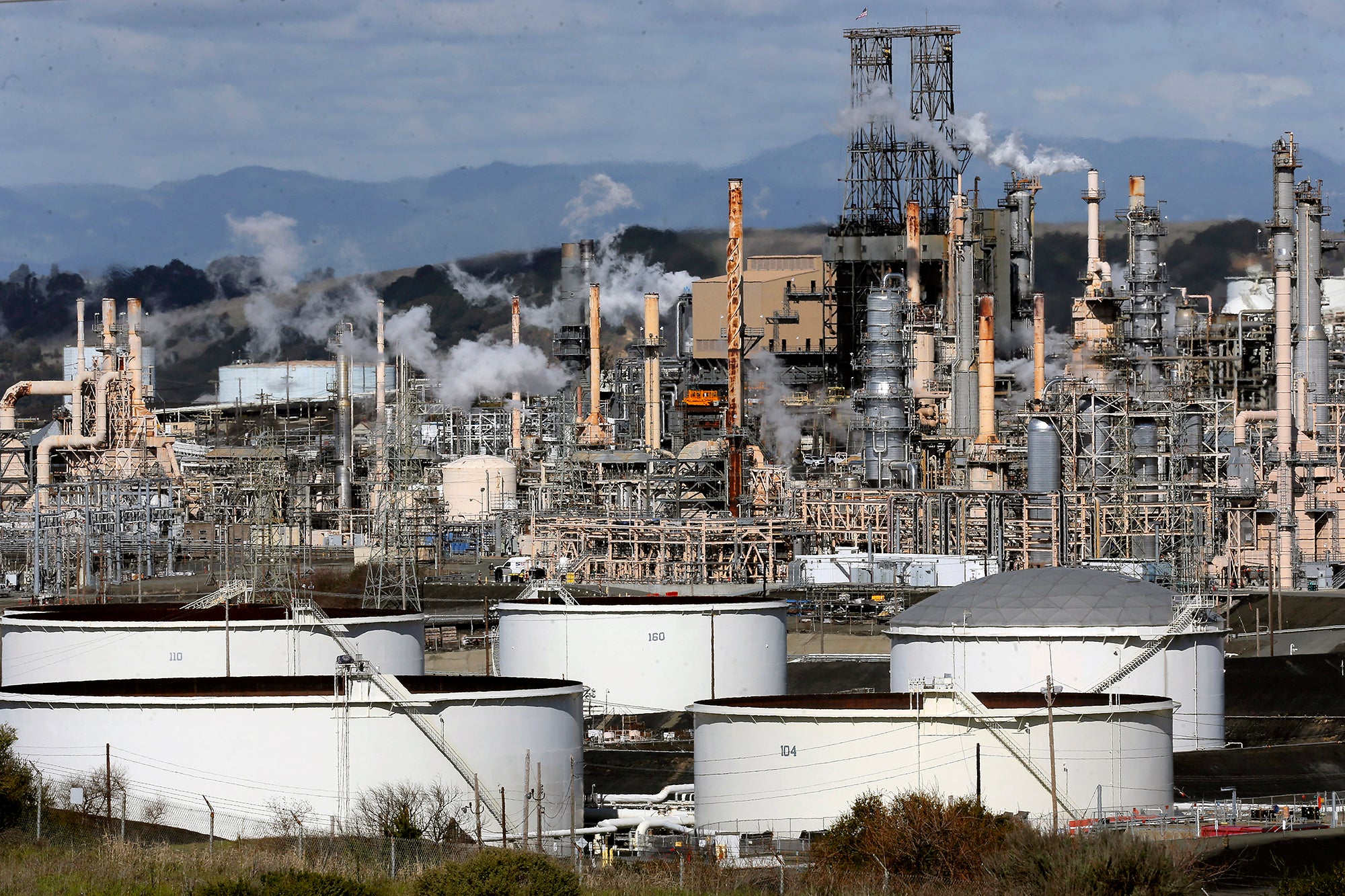 Large pipes, tanks and smokestacks with smoking coming out fill the frame of the photo.