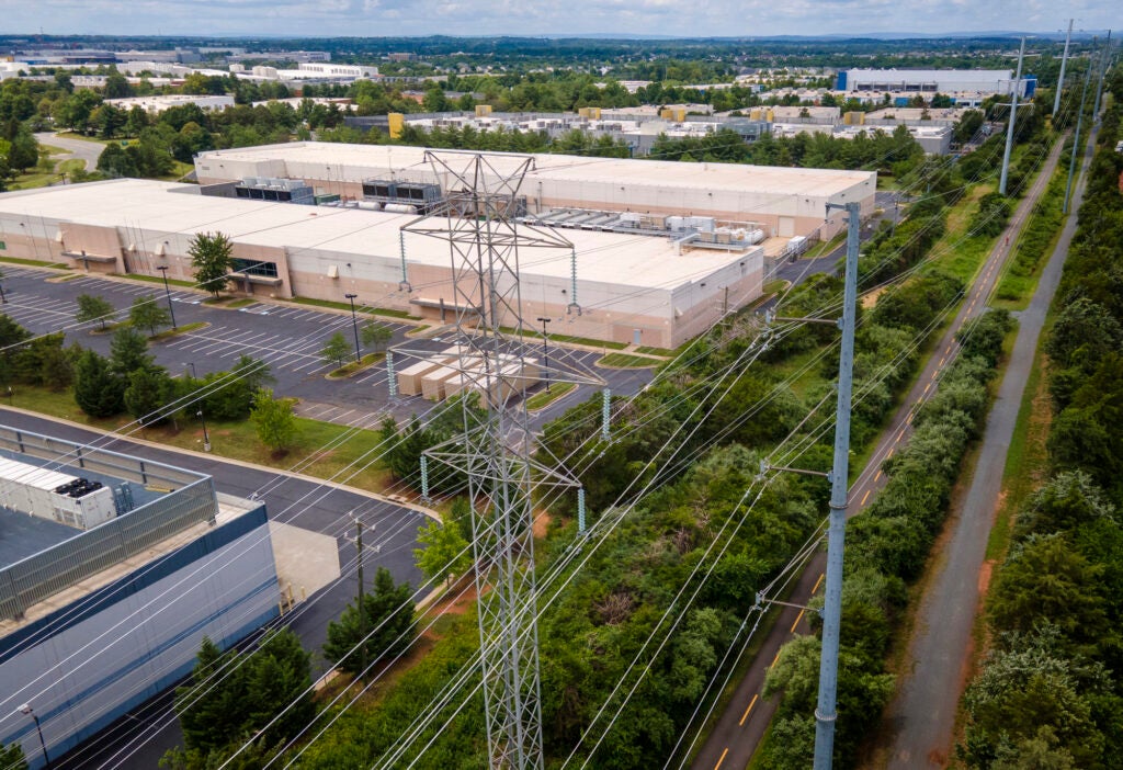 High-tension power lines cross in the foreground as large buildings lie in the background.