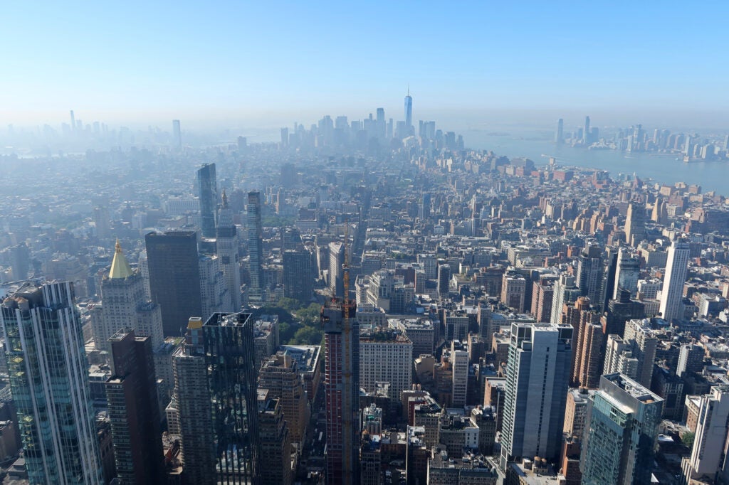 A wide cityscape of New York as seen from above. A gray haze covers the buildings below with a bluer sky above.