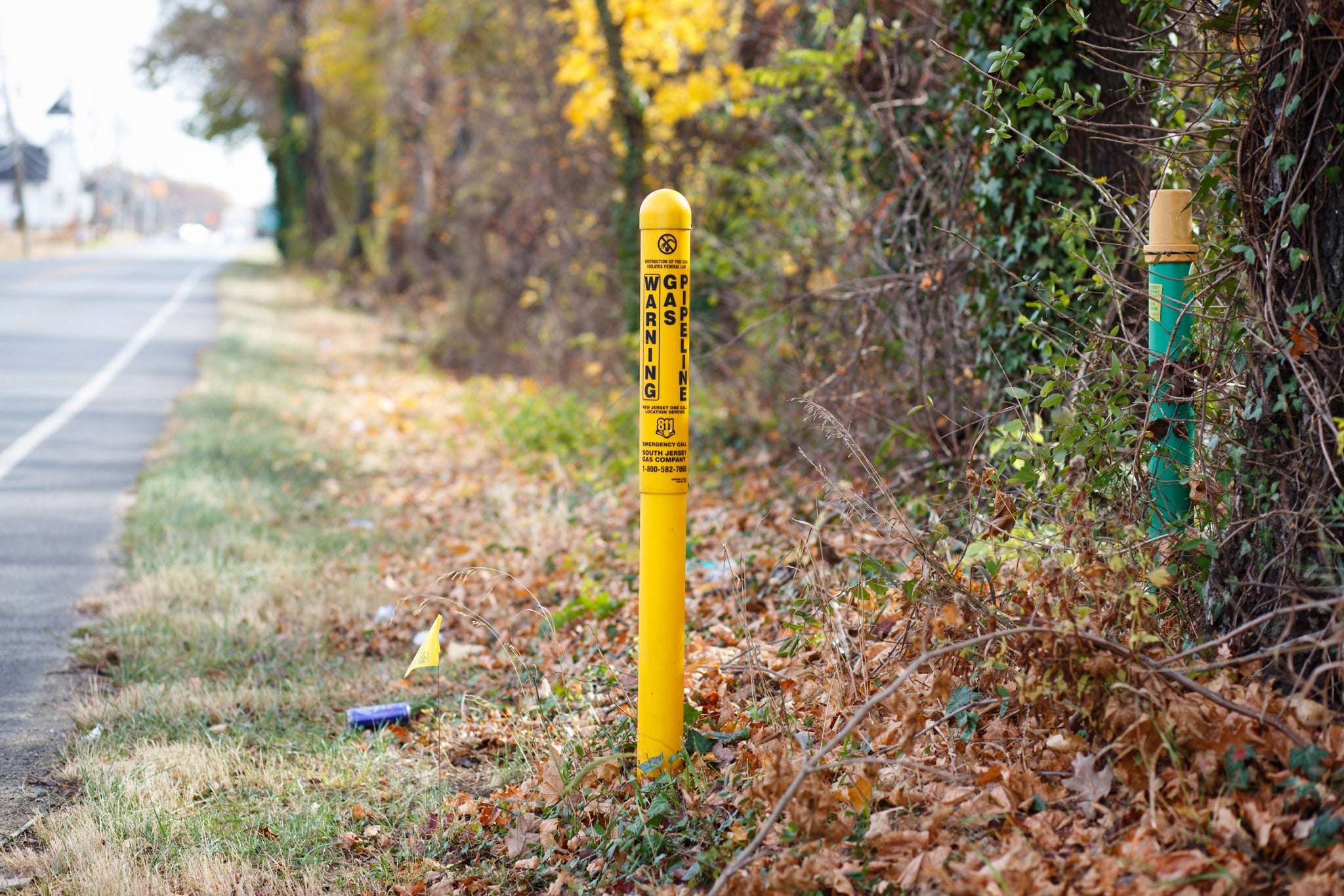 A short yellow post in the ground with the words "warning gas pipeline" written on it.