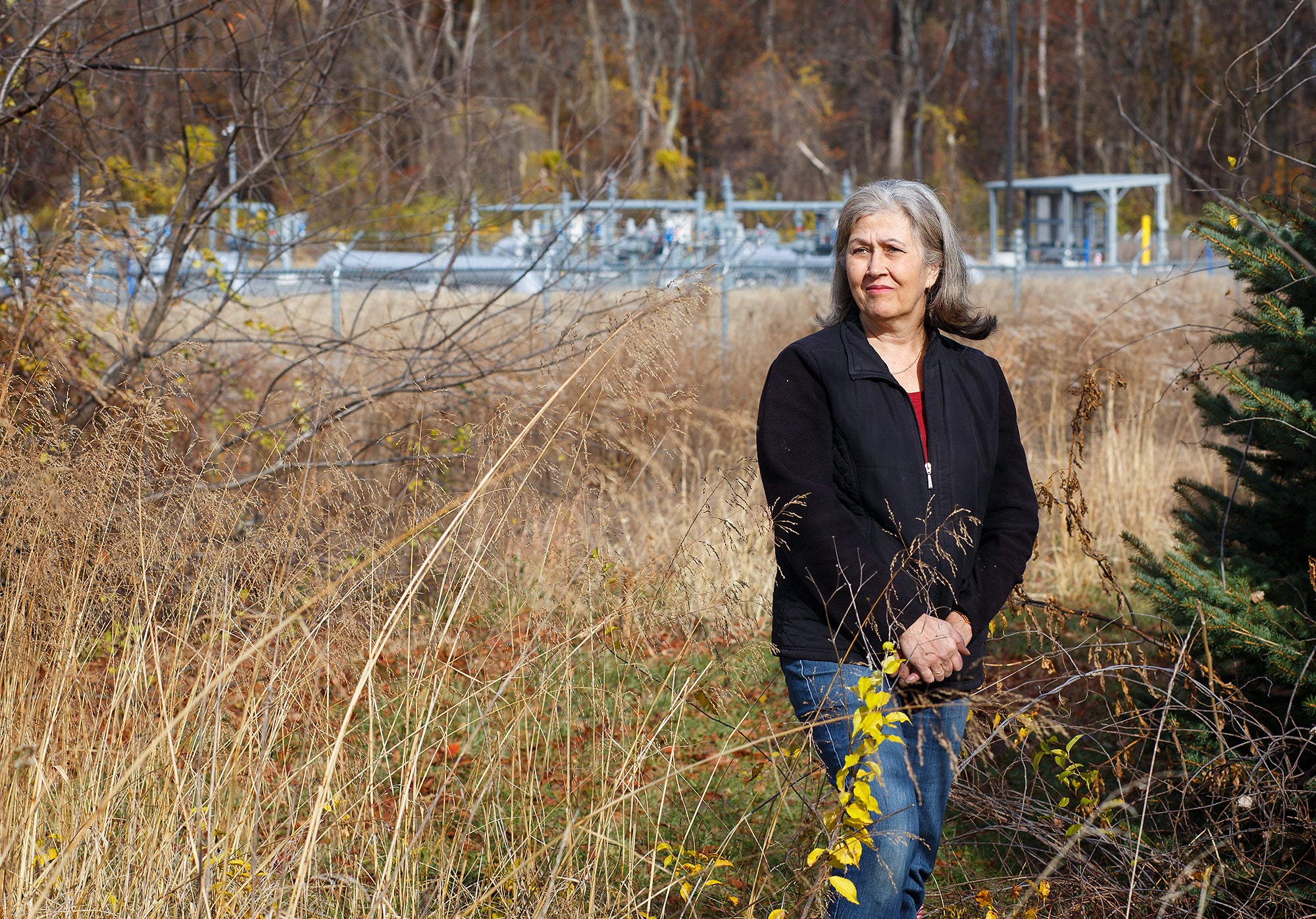 A woman stands in a field with methane pipeline infrastructure behind her