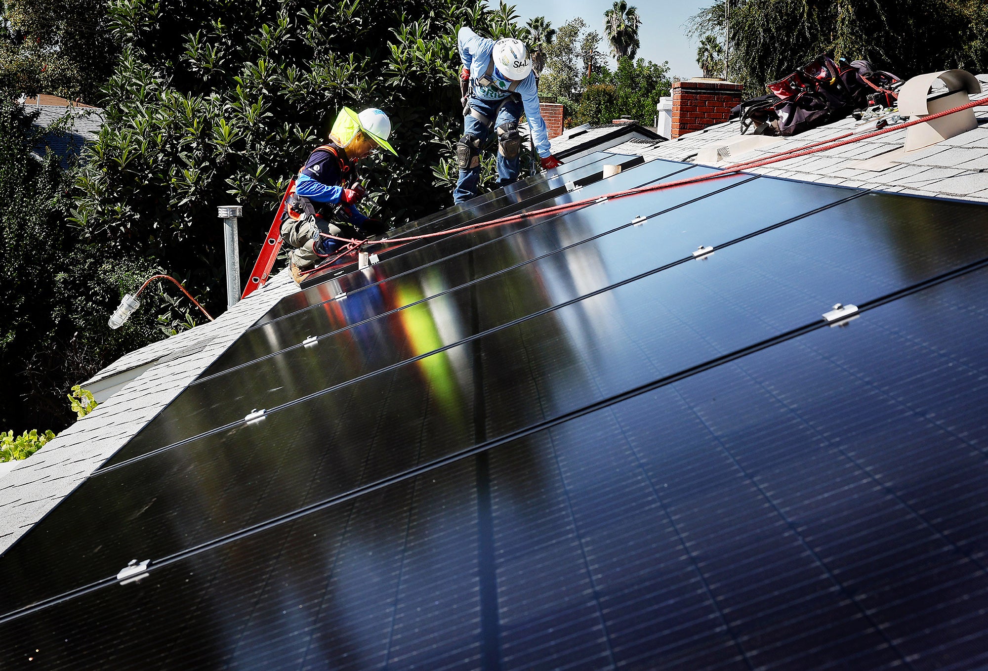 Two men install solar panels on the roof of a home on a clear day.