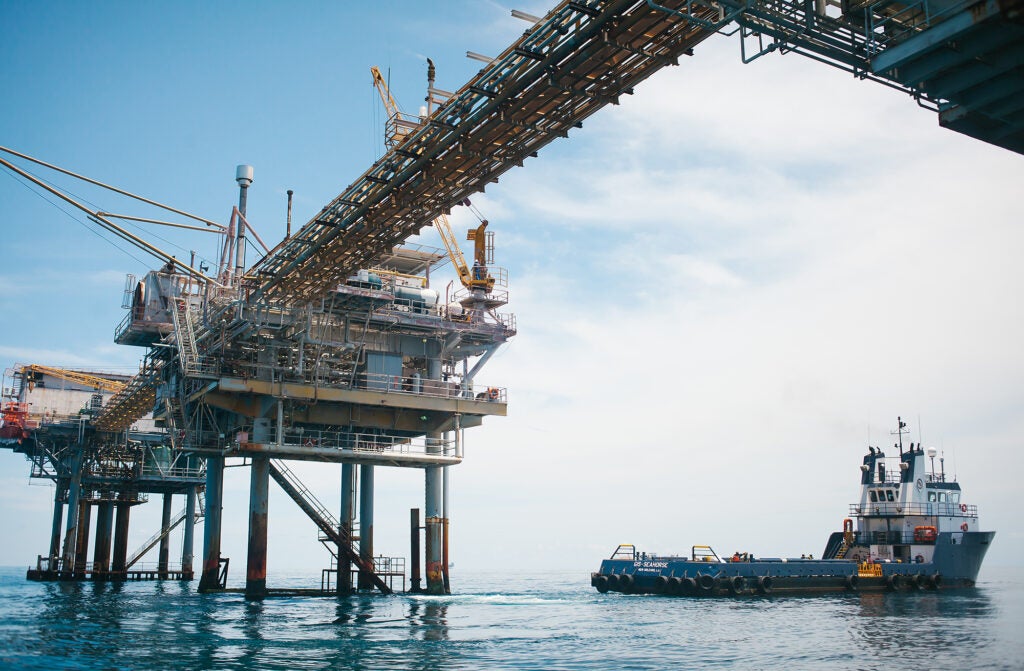 A photo just below an oil and gas rig in the ocean with a boat pulling away.