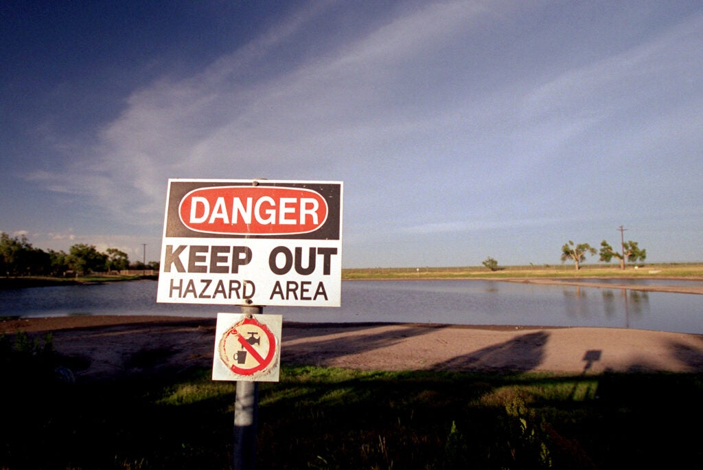 A sign saying "Danger Keep out, Hazard Area" with another signs indicating to not drink the water, is next to a small pond.