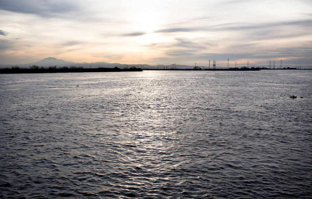 An body of water in the foreground of the photo with land and power lines in the middle distance and a mountain in the far distance.