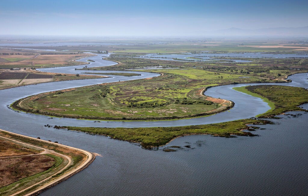 A large network of winding rivers and sloughs wrap around low green fields.