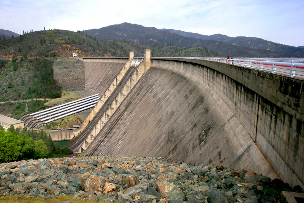 The dry side of a large concrete dam with a road on the top of it.