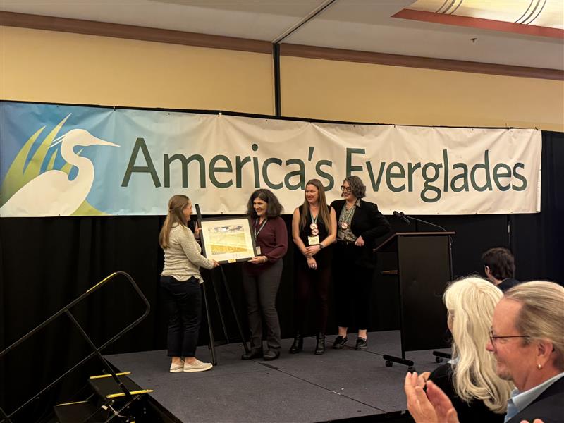 Three Earthjustice attorneys on stage receiving a framed award. "America's Everglades" written on a banner in the background.