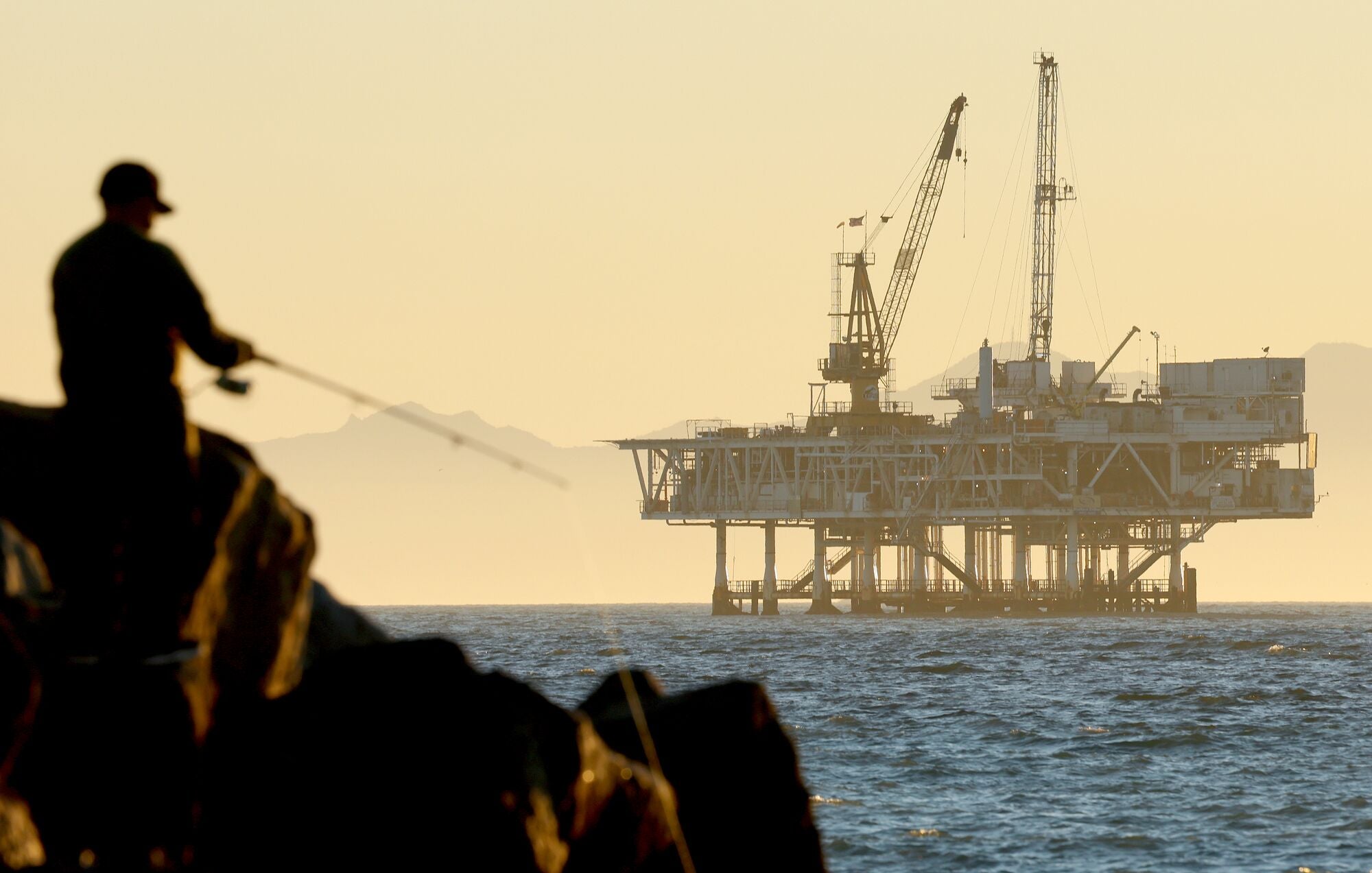 A person fishes with offshore oil and gas platform Esther in the distance on Jan. 5, 2025, in Seal Beach, California.