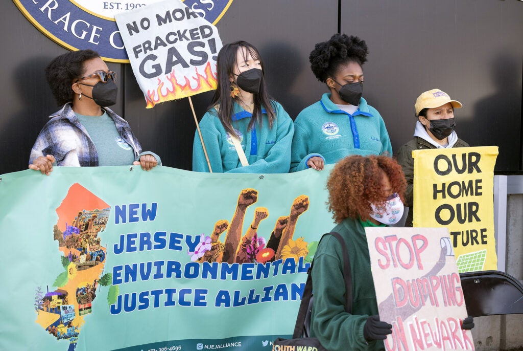 Five people hold signs for environmental justice and against pollution. Signs read "New Jersey Environmental Justice Alliance", Stop Dumping on Newark", "No more fracked gas!" and "Our home our future".