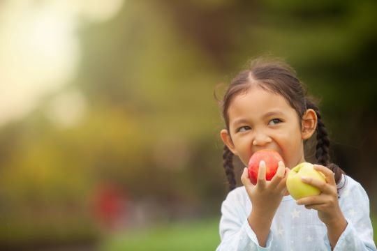 Close-up of girl eating apples near trees.