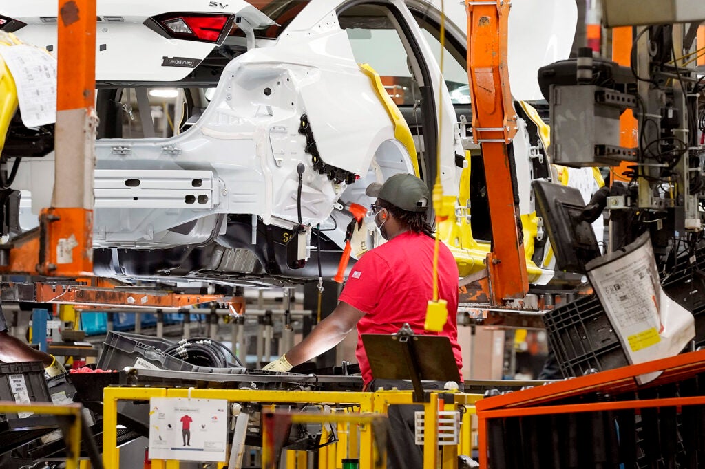 A person works on a white half-built car in a factory assembly line.