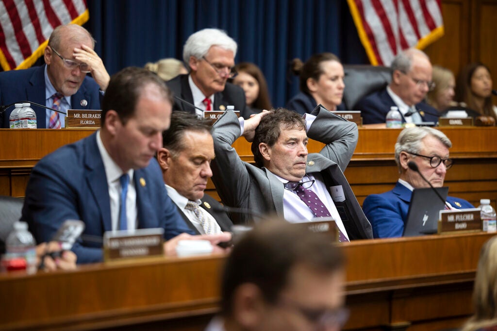 Multiple members of congress sit in rows in a hearing room listening to someone off camera. In this photo they are mostly men wearing suits and look very tired.