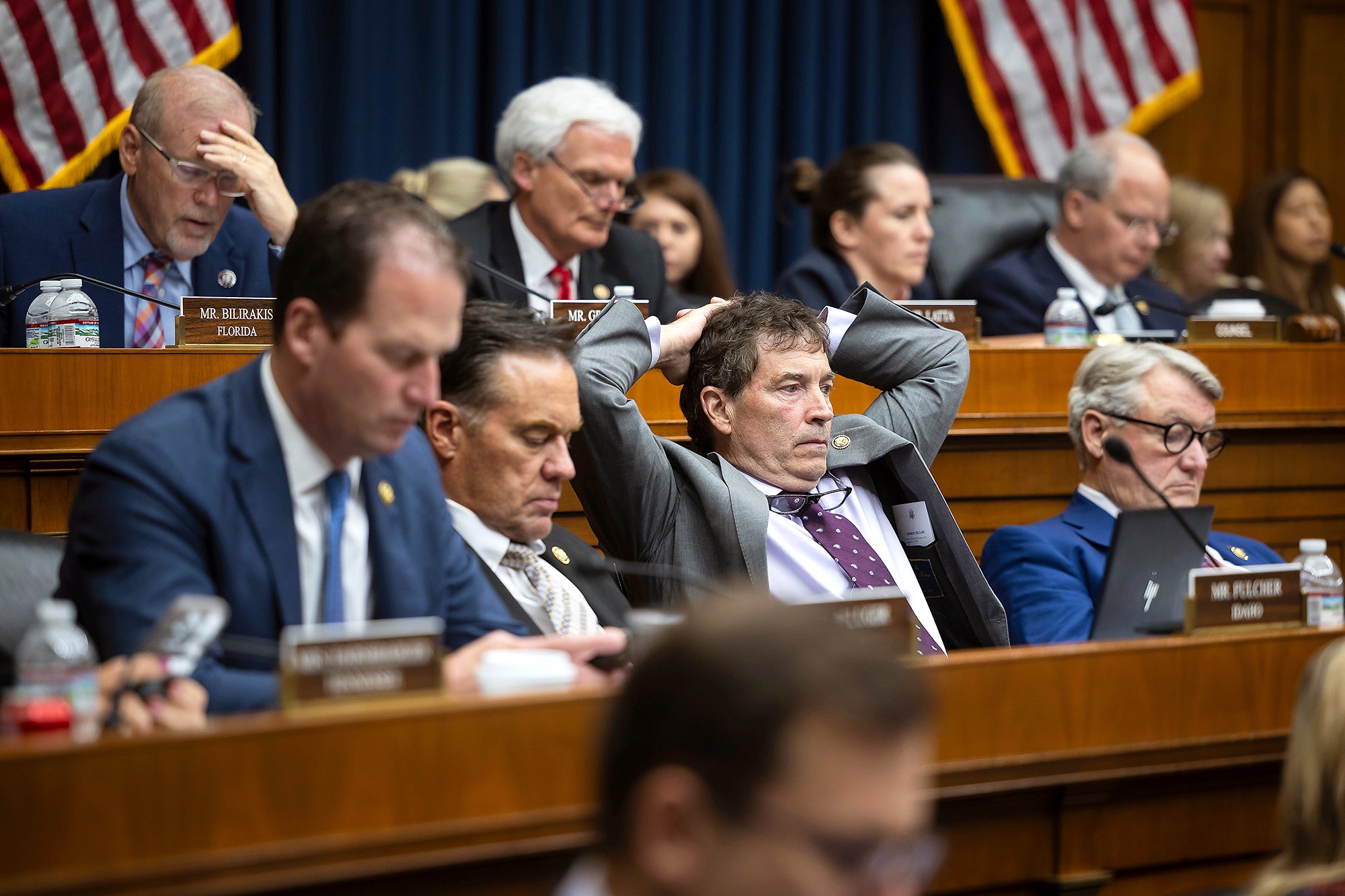 Multiple members of congress sit in rows in a hearing room listening to someone off camera. In this photo they are mostly men wearing suits and look very tired.