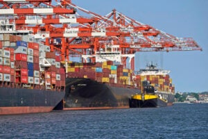 Cranes marked "Port Newark Container Terminal" and stacks of containers sit atop of ships in the water.