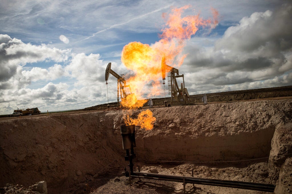 Flames come out of a metal pipe in a level dirt field with two pump jacks in the background.