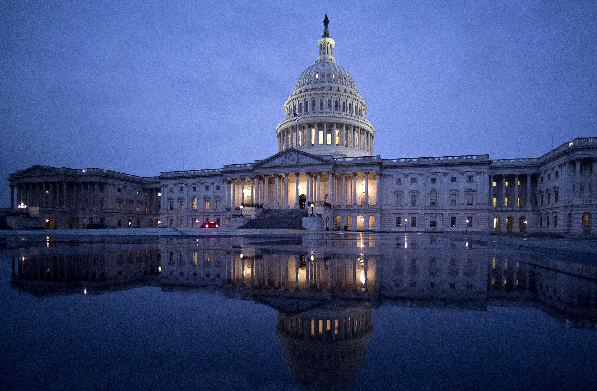 Reconciliation U.S. Capitol A wide photo of most of the U.S. Capitol building under a dark blue, cloudy sky. The building, with lights on, is reflected in water in the foreground.