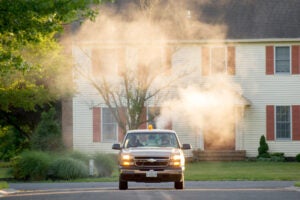 A truck drives in a residential area. Visible smoke or dust surrounds the truck.