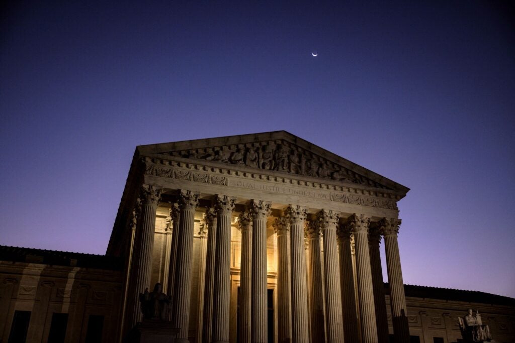 The front of the U.S. Supreme Court building, with its entrance brightly lit against a dark purple sky.