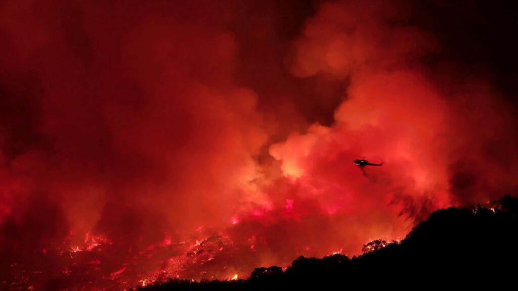 A helicopter extinguishing a wildfire on a mountain at night. (Konstantin Sutyagin / Getty Images)