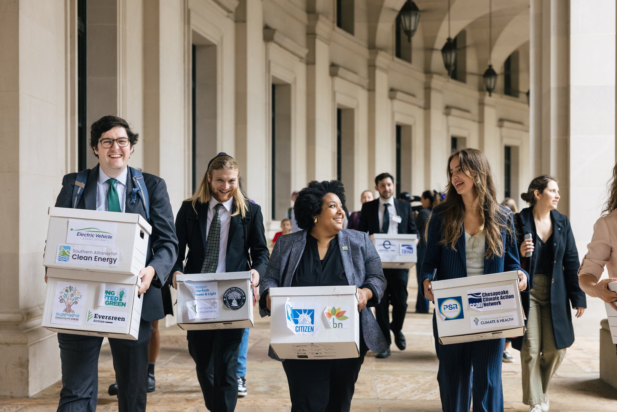 A group of people wearing suits carry white boxes next to a large government building.