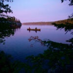 Two people in a canoe on still waters during twilight in the Boundary Waters Canoe Area in Northern Minnesota.
