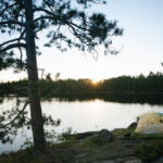 The sun peeks out over the top of the forest, illuminating a camp in the Boundary Waters Canoe Area.