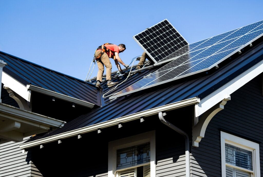 Two people on the roof of a home install solar panels.