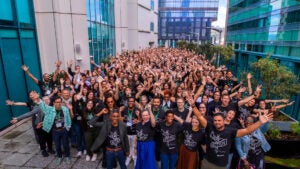 A large group (more than 500!) of friendly people wave and cheer for you from a courtyard lined with small trees. They are each wearing black t-shirts with a crossroads signpost design that has the words "Hope" and "Action".