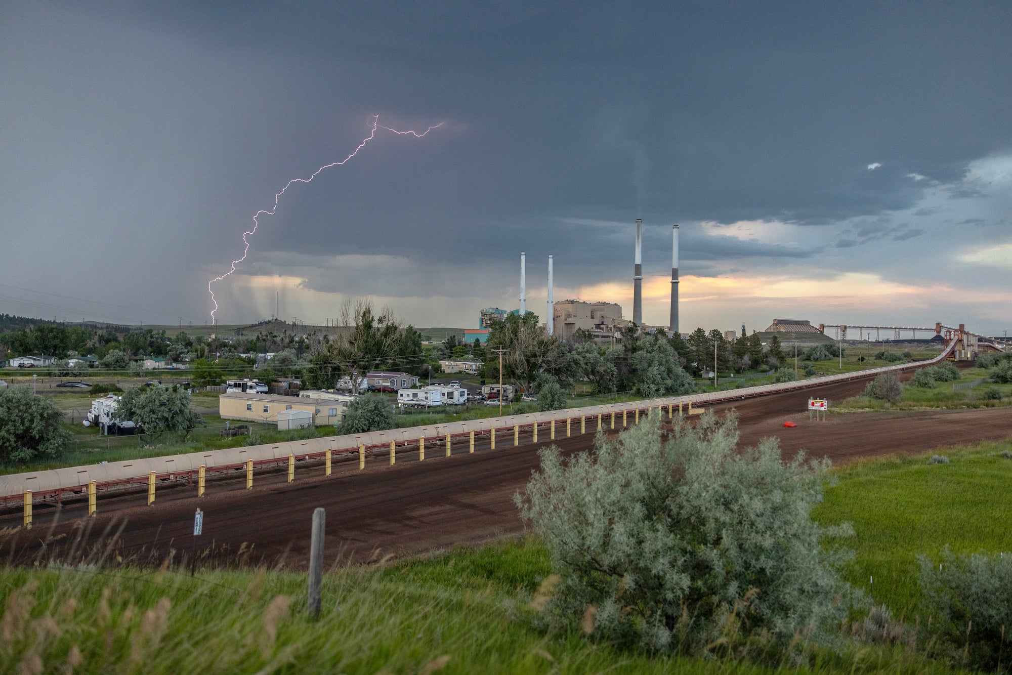 Lightning strikes in the distance beyond a power plant.