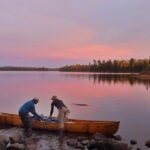 Two people reach for supplies in a kayak pulled close to shore in the Boundary Waters Canoe Area Wilderness.